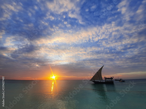 Calm indian ocean in the rays of the setting sun and blue sky with small clouds. a boat with a sail goes on the ocean.