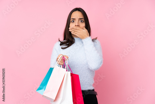 Young woman with shopping bag over isolated pink background covering mouth with hands