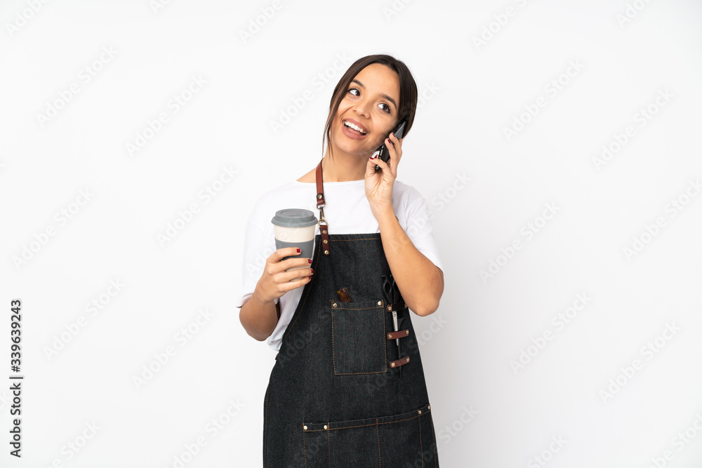 Young hairdresser woman isolated on white background holding coffee to take away and a mobile Young hairdresser woman isolated on white background holding coffee to take away and a mobile