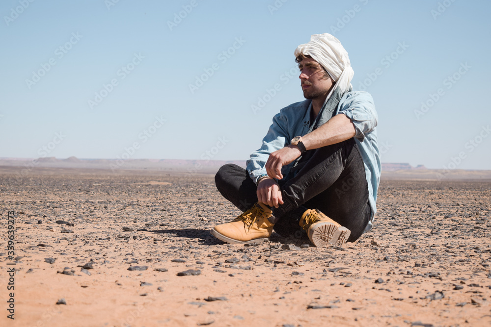 Viajero joven con turbante sentado en el desierto del Sahara Viajero joven con turbante sentado en el desierto del Sahara