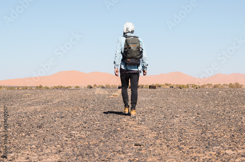 Viajero con turbante y mochila caminando hacia el horizonte en el desierto del Sahara en Marruecos