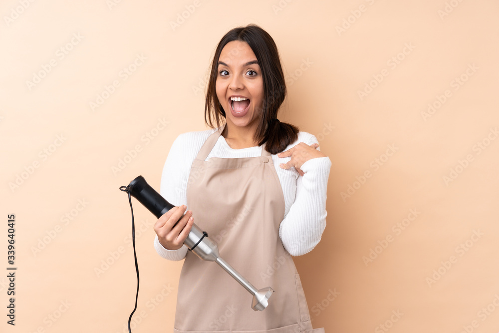 Young brunette girl using hand blender over isolated background with surprise facial expression Young brunette girl using hand blender over isolated background with surprise facial expression