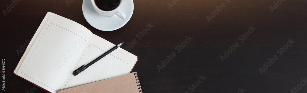 A Cup of coffee and an open notebook on the table. Long banner. The view from the top. A Cup of coffee and an open notebook on the table. Long banner. The view from the top.