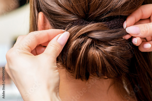 Hairdresser hands is making hairstyle for woman in beauty salon, close up, back view.