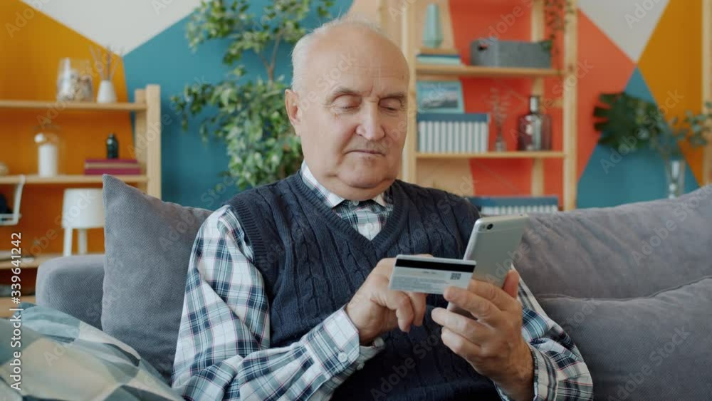 Retired man is shopping online making noncash payment with bank card and smartphone using electronic service at home. Retirement and gadgets concept. Retired man is shopping online making noncash payment with bank card and smartphone using electronic service at home. Retirement and gadgets concept.