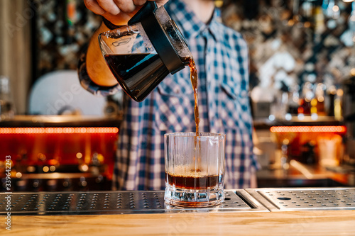 Alternative Coffee Brewing Method.  Close-up of the hands of barista  pouring a black filter coffee from a teapot into a transparent glass on a bar counter in a cafe.