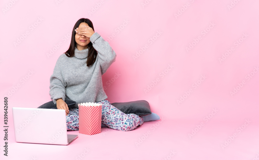 Young mixed race woman eating popcorn while watching a movie on the laptop covering eyes by hands. Do not want to see something Young mixed race woman eating popcorn while watching a movie on the laptop covering eyes by hands. Do not want to see something