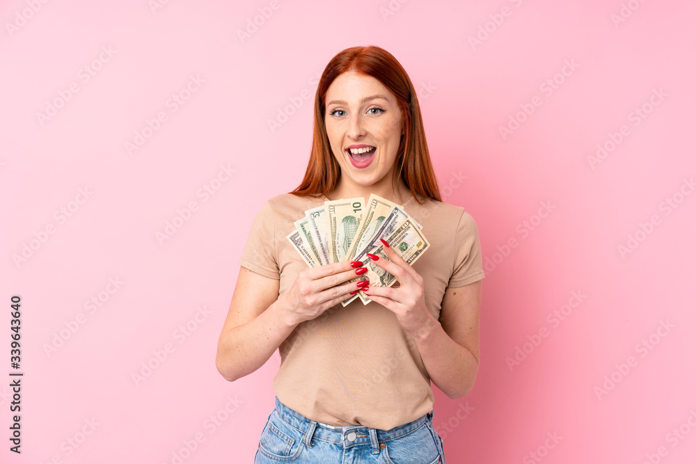 Young redhead woman over isolated pink background taking a lot of money Young redhead woman over isolated pink background taking a lot of money