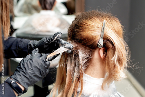 Hairdresser hands is dyeing hair of woman wearing black gloves in hair salon. Coloring hair.