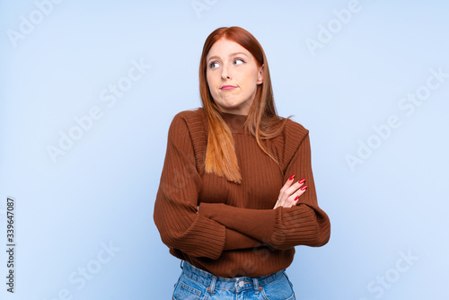 Young redhead woman over isolated blue background making doubts gesture while lifting the shoulders