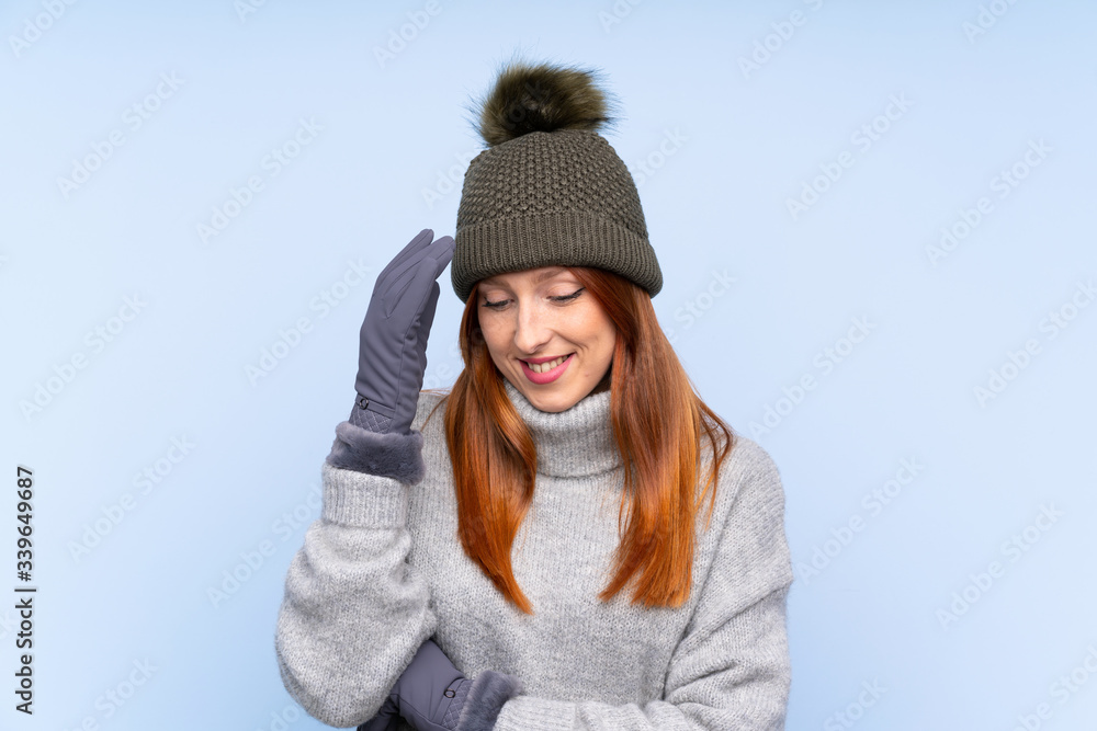 Young redhead Russian woman with winter hat over isolated blue background laughing Young redhead Russian woman with winter hat over isolated blue background laughing