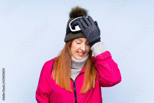 Skier redhead woman with snowboarding glasses over isolated blue wall having doubts with confuse face expression © luismolinero