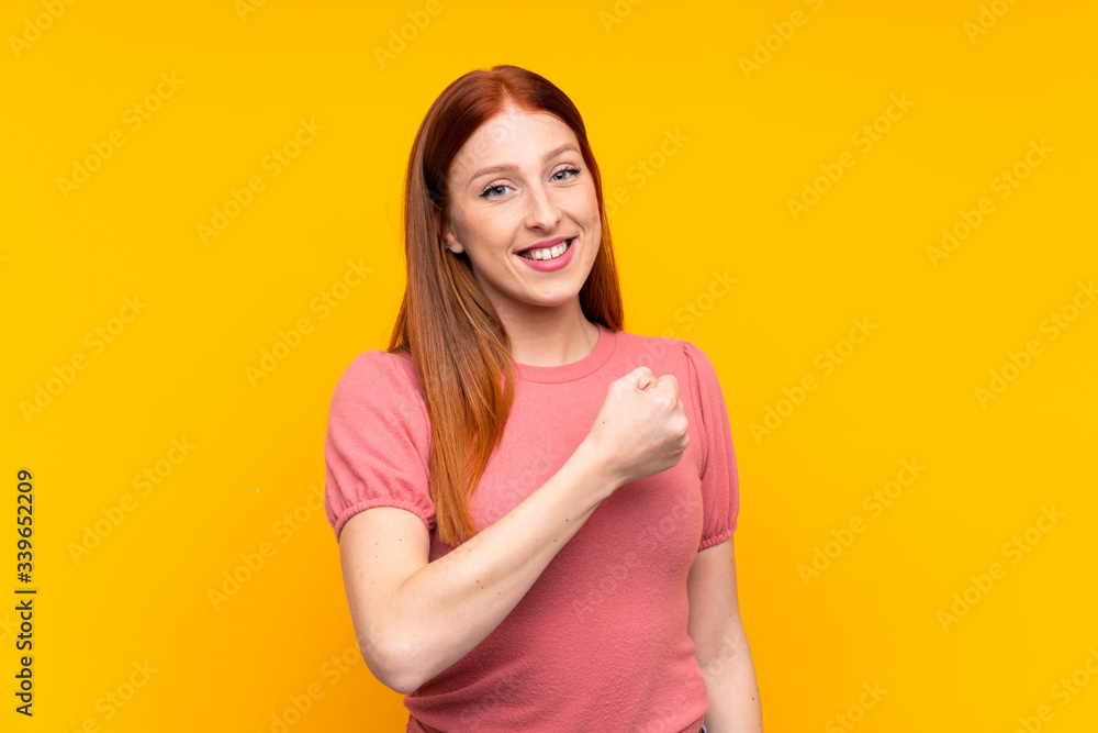 Young redhead woman over isolated yellow background celebrating a victory Young redhead woman over isolated yellow background celebrating a victory