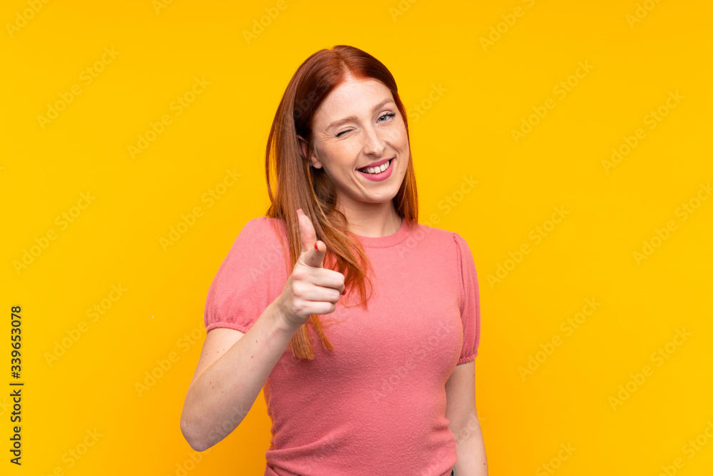 Young redhead woman over isolated yellow background points finger at you Young redhead woman over isolated yellow background points finger at you