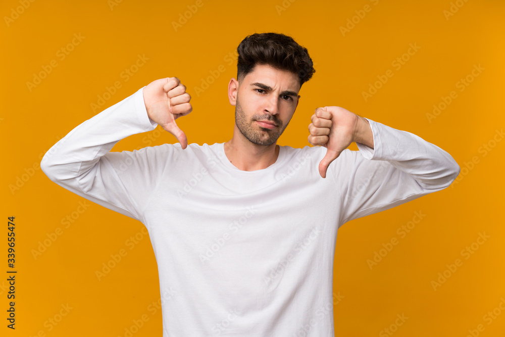 Young man over isolated orange background showing thumb down Young man over isolated orange background showing thumb down