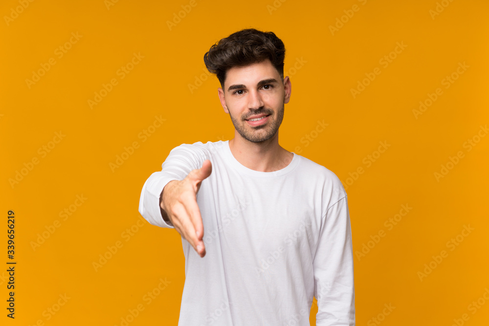 Young man over isolated orange background shaking hands for closing a good deal Young man over isolated orange background shaking hands for closing a good deal