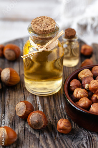 Concept of organic vegetable oils for cooking and cosmetology. Hazelnut nuts to illustrate ingredients. Rustic wooden background, natural oil in glass bottles. Close up, macro