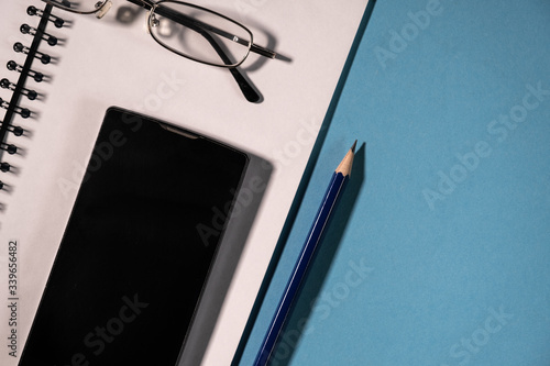 Obraz na płótnie top view of black cell phone, pencils and school notebook, glasses and spiral notepad on a table