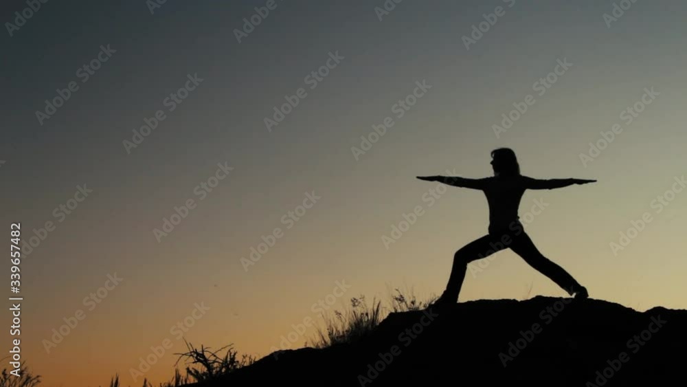 Silhouette of woman practicing in the yoga pose at the top of the sky during sunset. Spiritual yoga pose on the top at sunrise in slow motion Silhouette of woman practicing in the yoga pose at the top of the sky during sunset. Spiritual yoga pose on the top at sunrise in slow motion