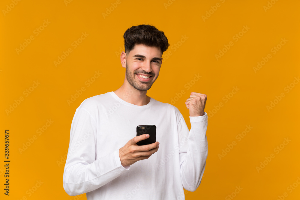 Young man over isolated orange background with phone in victory position Young man over isolated orange background with phone in victory position