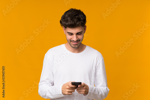 Young man over isolated orange background sending a message with the mobile