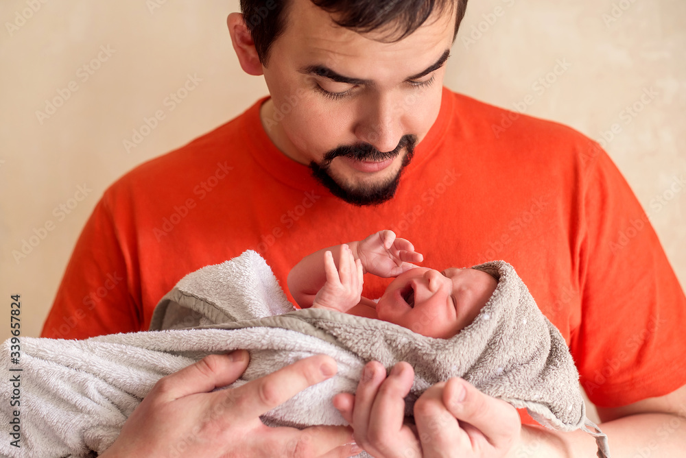 Young dad holding in arms infant baby girl wrapped in blanket, trying to  calm her down.