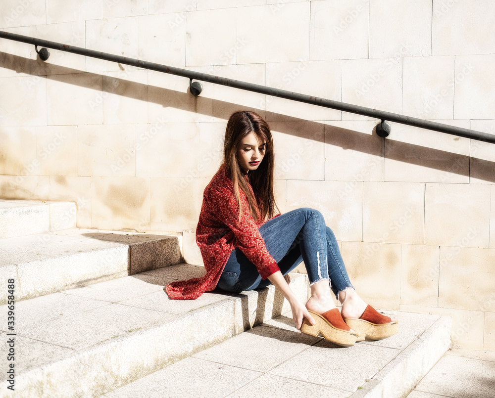 Beautiful young girl sitting on the stairs putting her shoe on Beautiful young girl sitting on the stairs putting her shoe on