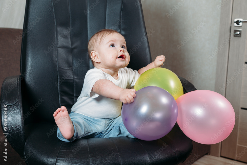 Obraz premium funny child sitting on chair little boy having fun playing big colored balloons