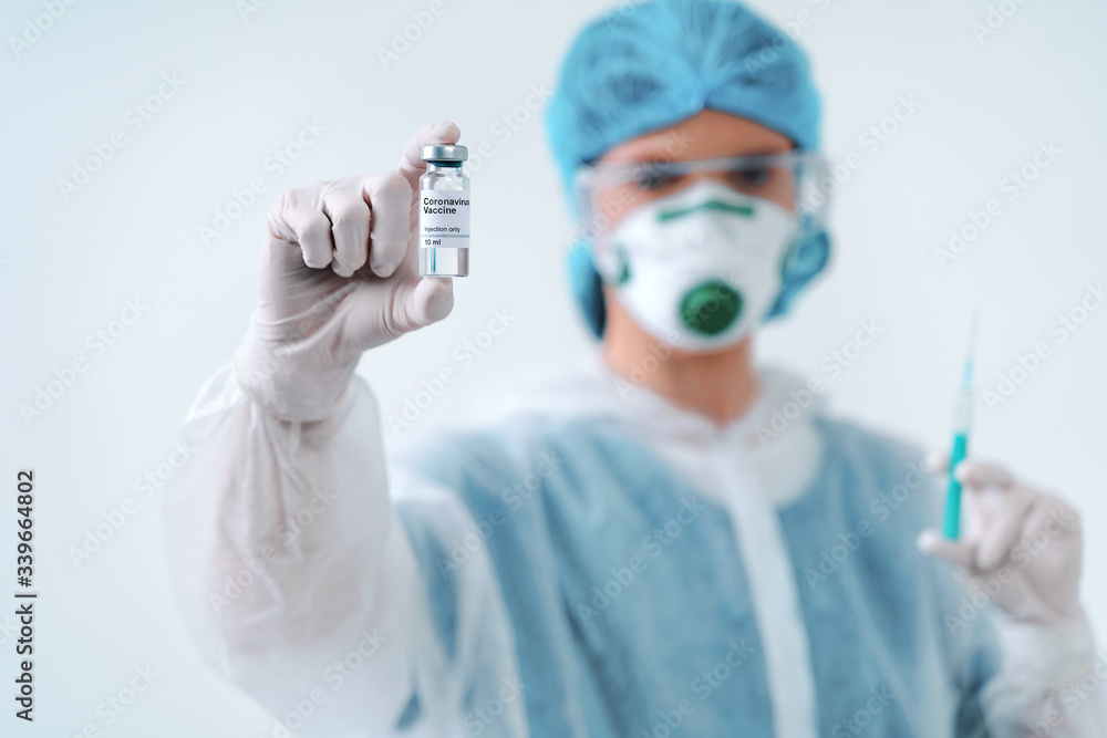 Nurse in protective suit and mask holds an injection syringe and vaccine. Biological hazard. Nurse in protective suit and mask holds an injection syringe and vaccine. Biological hazard.
