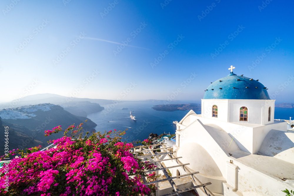 Obraz premium bougainvillea bloom and Beautiful blue dome church and view of voclanic caldera in Imerovigli, village on Santorini island, Cyclades, Greece