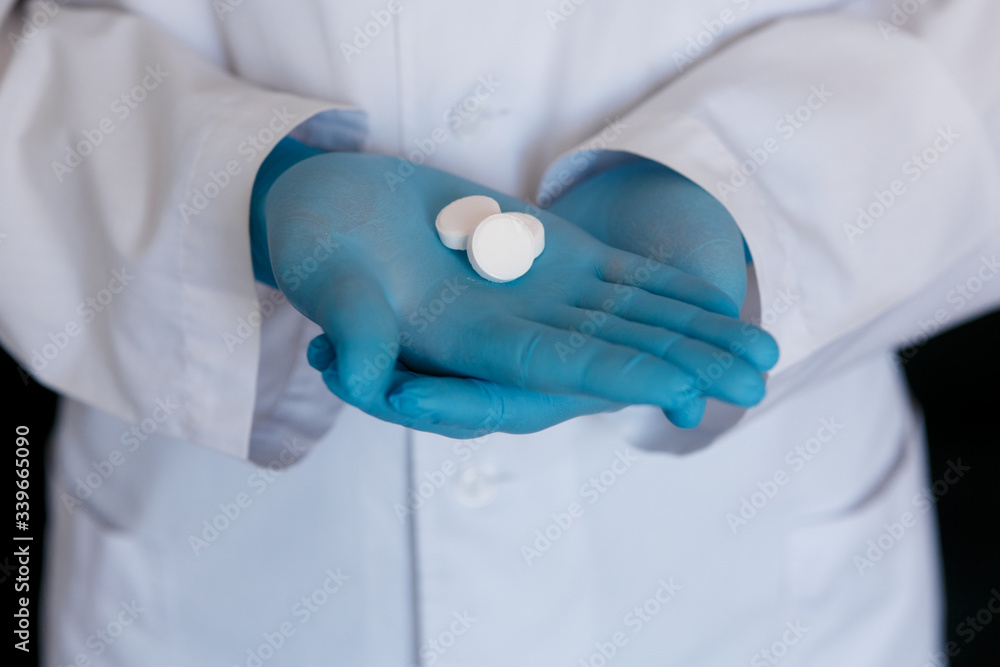Many small white pills in the hands of a doctor wearing medical blue disposable gloves. Hands take one pills Many small white pills in the hands of a doctor wearing medical blue disposable gloves. Hands take one pills