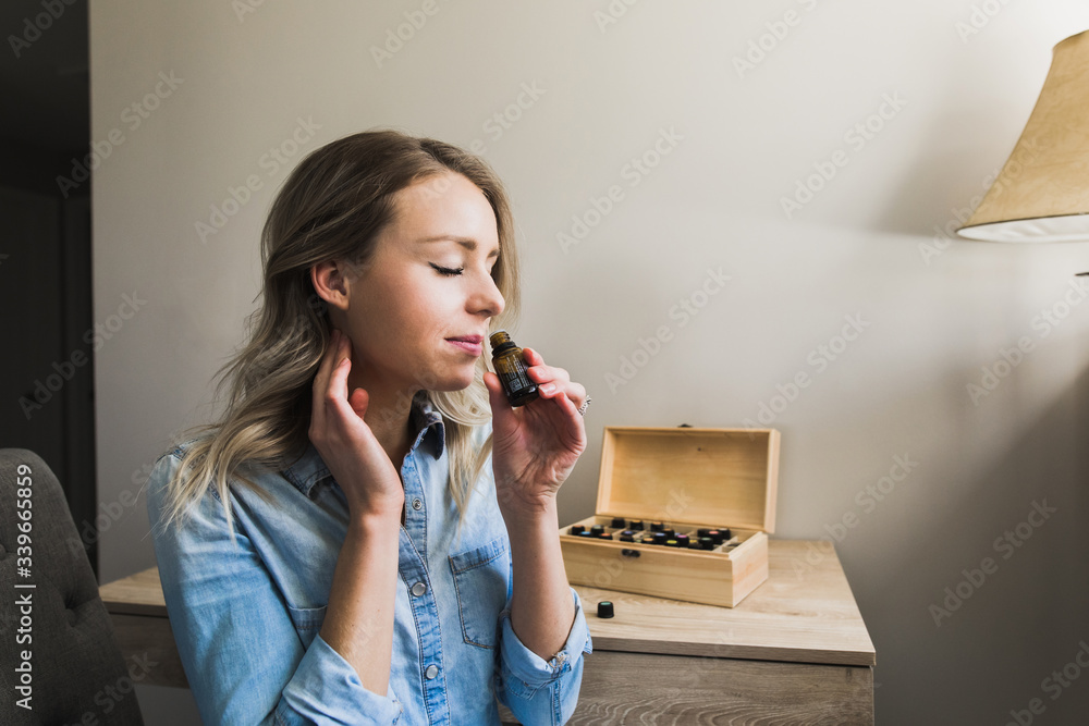 Young woman applying essential oils to her neck and smelling open bottle - obrazy, fototapety, plakaty 