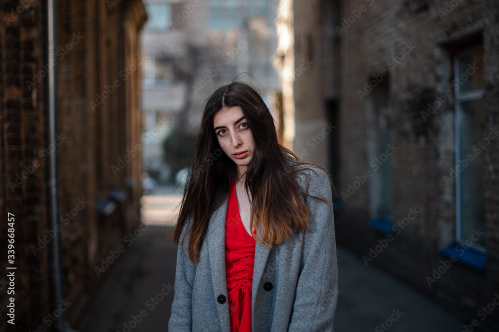 Fototapeta premium Girl in a red blouse and a gray cardigan on the background of the old brick wall