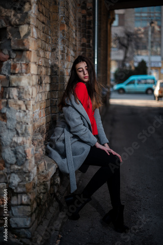 Girl in a red blouse and a gray cardigan on the background of the old brick wall