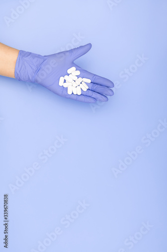 Hands in blue medical gloves hold handful white pills on light blue background. Minimal medical concept. Flat lay, top view, copy space