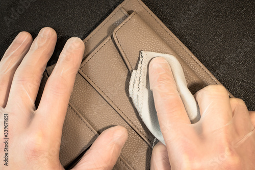 Male hands in disposable gloves erase fingerprints from an opened wallet on a black background. Gloved hands disinfect the wallet.