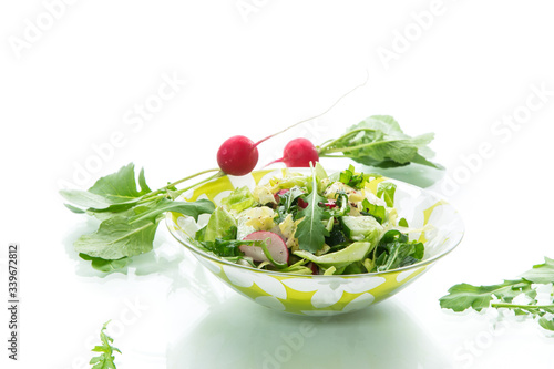 Spring salad from early vegetables, lettuce leaves, radishes and herbs in a plate isolated on white