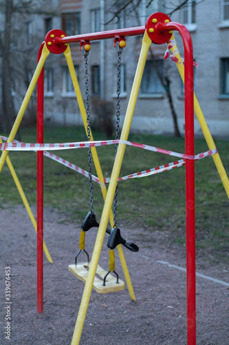 The playground and the swing for children are closed and blocked by a barrier tape due to the covid19 crown virus. A swing on the court cannot be used. Nobody on the swing.