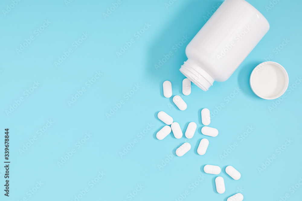 White pills spilled out of white bottle on light blue background. Minimal medical concept. Flat lay, top view, copy space White pills spilled out of white bottle on light blue background. Minimal medical concept. Flat lay, top view, copy space