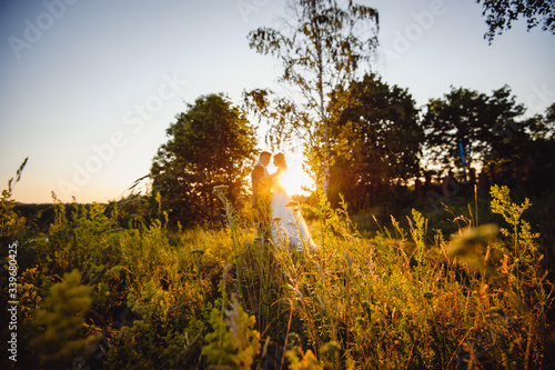Silhouettes of brides on sunset, which stand among dense vegetation and trees. Wedding photo shoot.