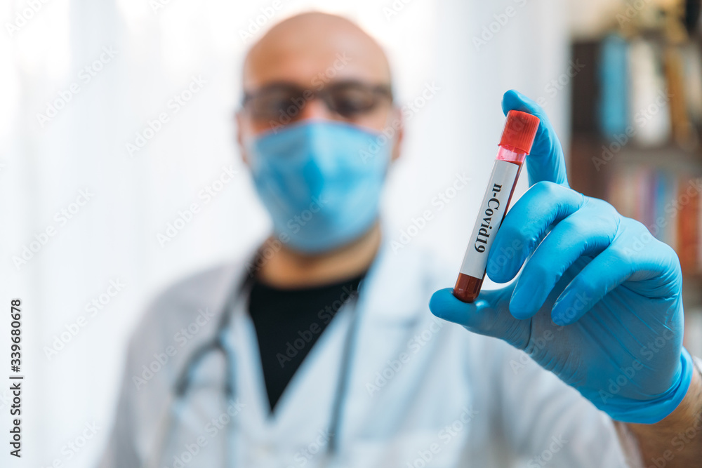 Doctor Holding Pandemic Coronavirus 2019-nCoV Blood Sample Positive Test Tube. Doctor wearing medical mask and gloves and shows patient's blood test tube containing corona virus (COVID-19) Doctor Holding Pandemic Coronavirus 2019-nCoV Blood Sample Positive Test Tube. Doctor wearing medical mask and gloves and shows patient's blood test tube containing corona virus (COVID-19)