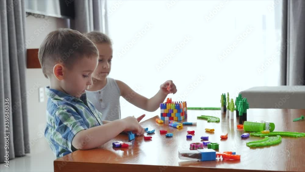 Happy family, a daughter and a son, two small children at home sit at a table and play in the constructor, build a tower, playful children help each other, having fun playing with toys in the living Happy family, a daughter and a son, two small children at home sit at a table and play in the constructor, build a tower, playful children help each other, having fun playing with toys in the living