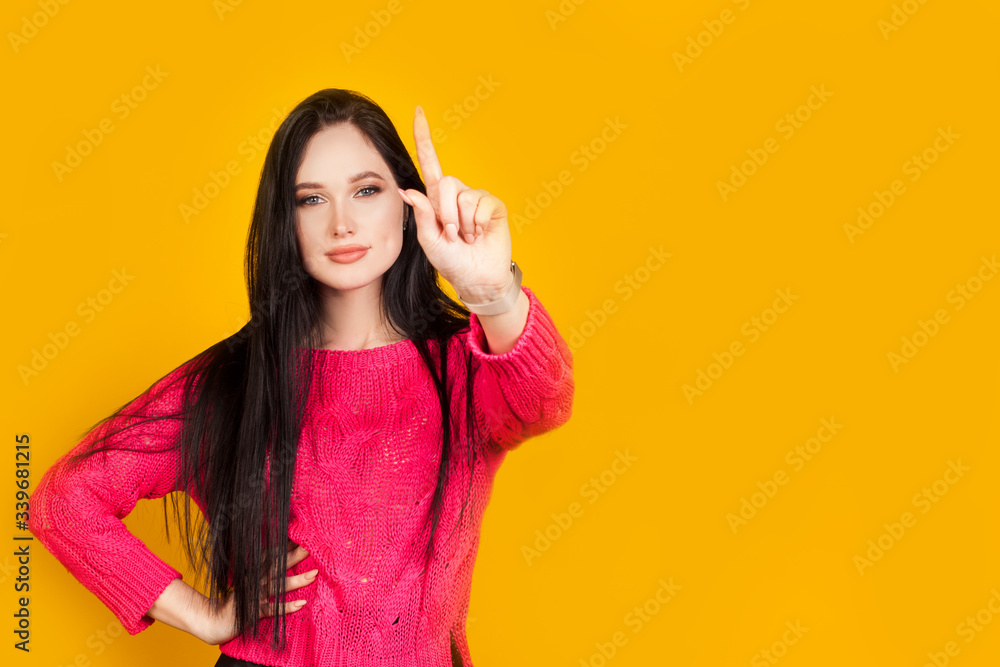Index finger up, the girl holds on a yellow background, with copy space. Concept valuable guidance, first step or first action, important information. Index finger up, the girl holds on a yellow background, with copy space. Concept valuable guidance, first step or first action, important information.