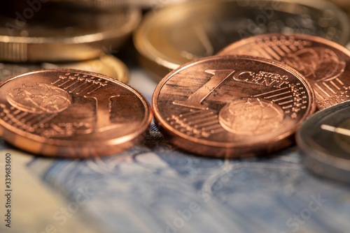 Closeup of 1 Euro cent coin on top of blue 20 euro bill. One Euro coin out of focus in the background. Shortage of money