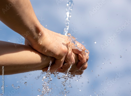 Clear Water flows down on men's hands against the sky.
