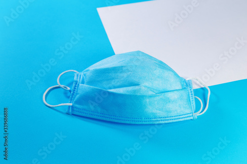 white sheet of paper and medical mask on blue background with copy space. Medical background