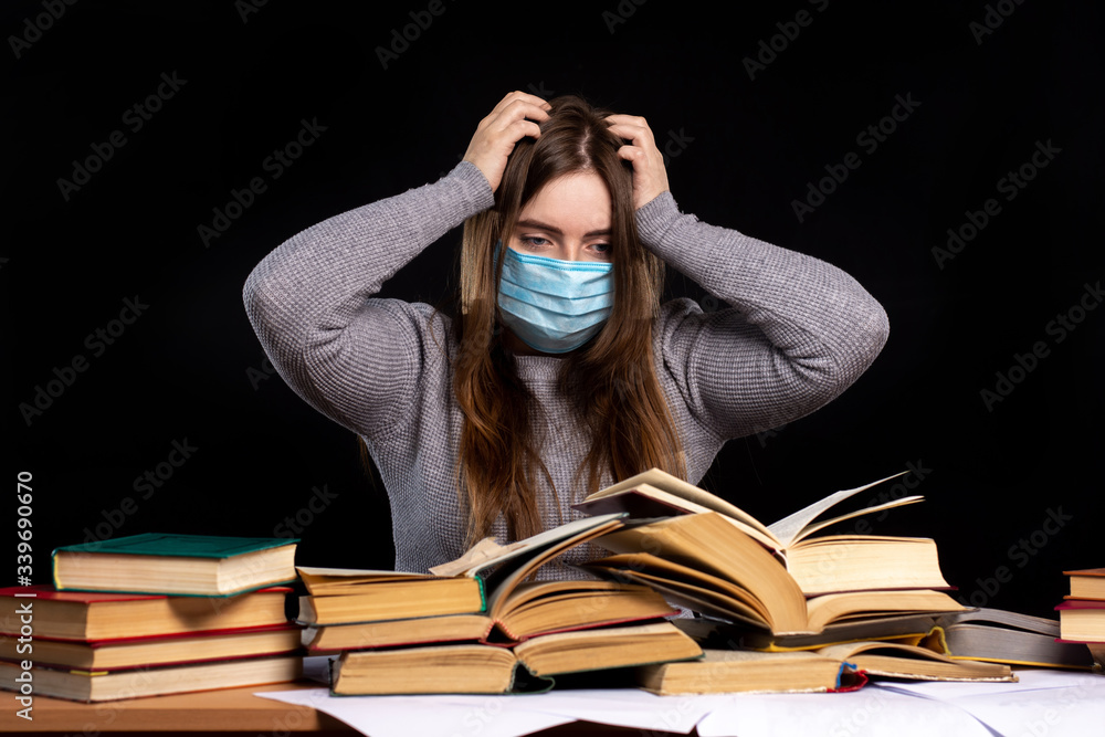 a young girl in a medical mask sits against a black wall behind stacks of books. self-education a young girl in a medical mask sits against a black wall behind stacks of books. self-education