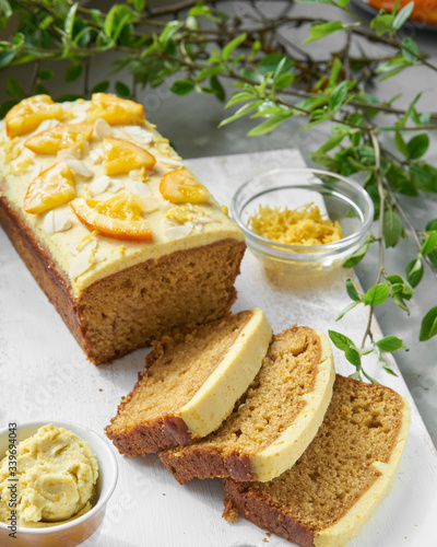 Vegan orange loaf cake and slices.Homemade citrus cake with white cashew cream on top. Green spring leaves around.