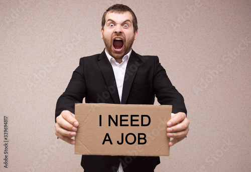 concept unemployment and coronavirus a man in black suit is holding a cardboard tablet with the inscription need a job. unemployment and crisis concept.