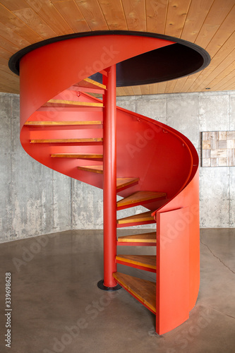 Red circular staircase between a concrete floor and a wooden ceiling